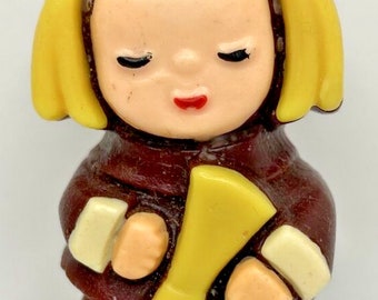 May include: A vintage candle in the shape of a firefighter. The candle is mainly maroon with yellow and cream-coloured accents. The firefighter has closed eyes, red lips, and yellow hair. The candle is standing upright.