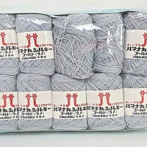May include: A package of light gray yarn skeins. Each skein is wrapped with a white label featuring Japanese text and a floral design. The yarn appears to be a blend of silk and other fibers.