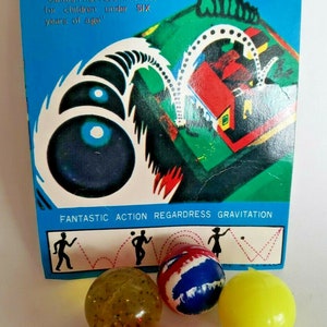 May include: A vintage "Hi-Bouncing Ball" toy set with a blue and white box featuring graphics and text. The set includes several colorful bouncy balls in yellow, red, blue, and a striped ball. The box warns against use by children under six.