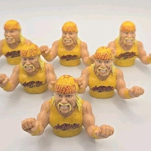 May include: Six yellow and tan figurines of a wrestler with a blonde mustache and headband. The figurines are wearing yellow tank tops and have the word "Hogan" on their headbands. The word "Hulkster" is printed on the tank tops.