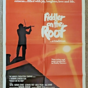 May include: Vintage movie poster for "Fiddler on the Roof" with a silhouette of a violinist on a rooftop against an orange and yellow background. The title is in large white letters, with additional text.