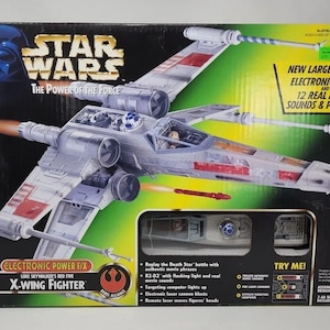 May include: A boxed Star Wars X-Wing Fighter toy. The box features the Star Wars logo and Darth Vader. The toy is a detailed model with electronic lights and sounds. The box also includes text that says "Electronic Power F/X" and "Luke Skywalker's Red Five X-Wing Fighter".