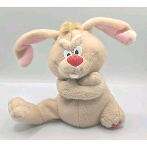 May include: A plush rabbit toy with tan fur, long ears with pink inner lining, and a tuft of hair on its head. It has a shiny red nose, white buck teeth, and a grumpy facial expression with furrowed brows. Its arms are crossed over its chest.