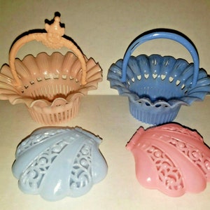 May include: Four small, decorative baskets and shell-shaped lids in pastel colors. Two baskets have handles, one peach-colored with a crown-like detail, and one blue. The shell lids are light blue and pink, with intricate cut-out designs.