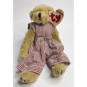 May include: A tan plush teddy bear wearing a red and white striped outfit. The bear has a black nose and a Ty collectible tag attached. The outfit includes a dress and pants.