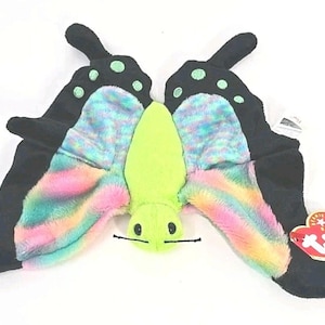 May include: A plush butterfly toy with black wings featuring green polka dots. The wings have a rainbow-colored, fluffy interior. The body is lime green with black antennae. A red heart-shaped tag is attached.