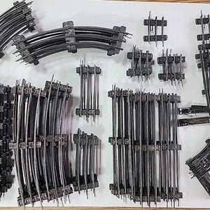 May include: A collection of black plastic model train track pieces. The track pieces are arranged in a variety of configurations, including curves, straights, and switches.