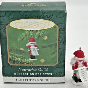 May include: A Hallmark Keepsake Ornament featuring a Nutcracker Guild Santa Claus holding a list with names on it. The ornament is part of the Collector's Series and is from the year 2000.