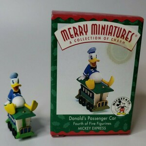 May include: A miniature figurine of Donald Duck in a blue sailor suit and hat, seated on a green and white passenger car. The figurine is next to a box with the text "MERRY MINIATURES" and "Donald's Passenger Car".