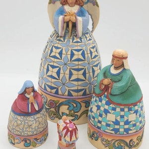 May include: A set of four hand-painted ceramic figurines depicting the Nativity scene. The figures include a blue-robed angel holding a star, a woman in a red robe, a woman in a green robe, and a baby in a pink and white blanket.