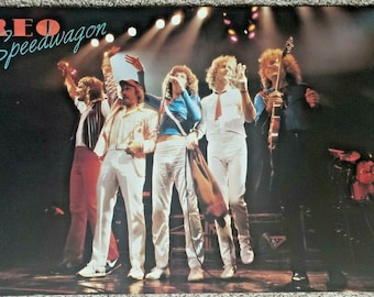 May include: A vintage concert poster featuring the band REO Speedwagon. The poster shows the band members on stage performing in front of a dark background with spotlights. The band members are wearing white clothing and are holding musical instruments.