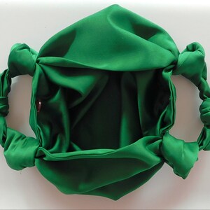 May include: A green satin fabric bag with two knotted handles. The bag is empty and open, showing the inside of the fabric.
