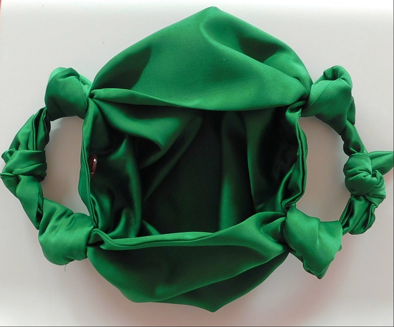 May include: A green satin fabric bag with two knotted handles. The bag is empty and open, showing the inside of the fabric.