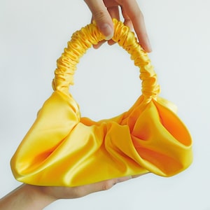 May include: A bright yellow satin handbag with a gathered design and a single handle.