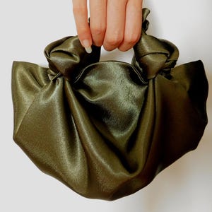 Pu&ograve; includere: Una borsa a mano in satin verde con un manico annodato.