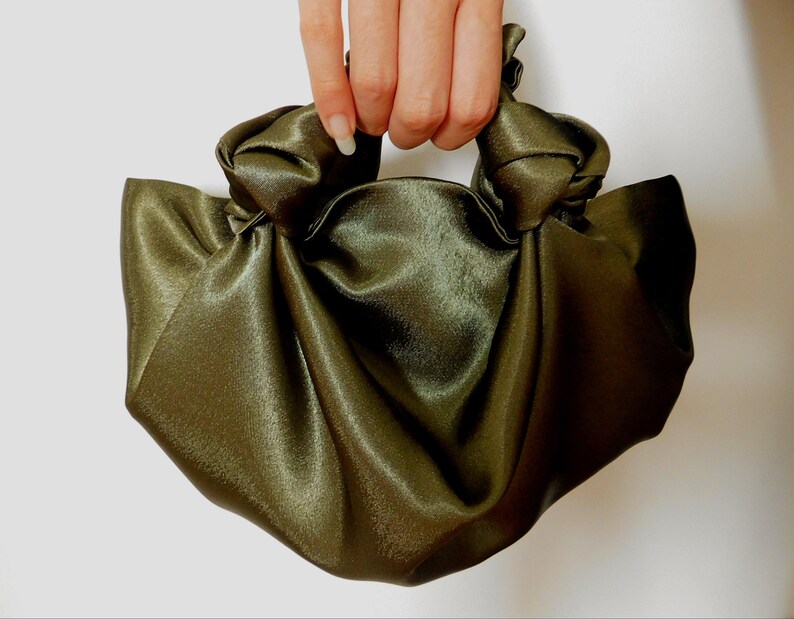 Pu&ograve; includere: Una borsa a mano in satin verde con un manico annodato.