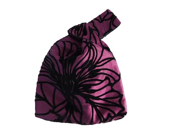Könnte beinhalten: Eine kleine, geknotete Handtasche in leuchtendem Magenta, verziert mit einem auffälligen schwarzen Blumenmuster. Das Design der Tasche zeichnet sich durch einen einzigartigen Griff und eine weiche, samtige Textur aus.