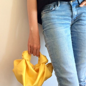 May include: A bright yellow knotted fabric handbag. The bag is made of a soft, silky material and has a simple, elegant design.