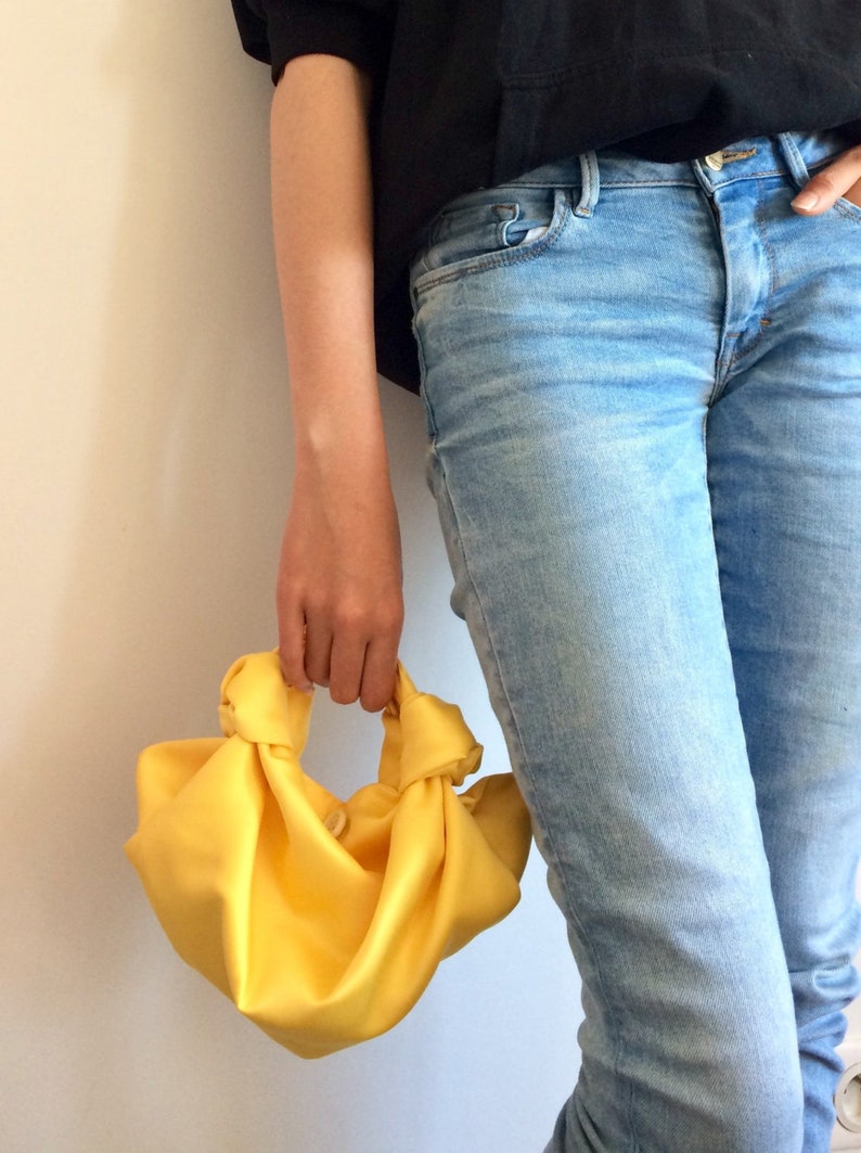 May include: A bright yellow knotted fabric handbag. The bag is made of a soft, silky material and has a simple, elegant design.