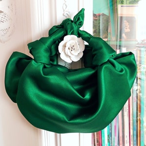 May include: A green satin handbag with a white flower accent. The bag is gathered and knotted to create a unique shape.