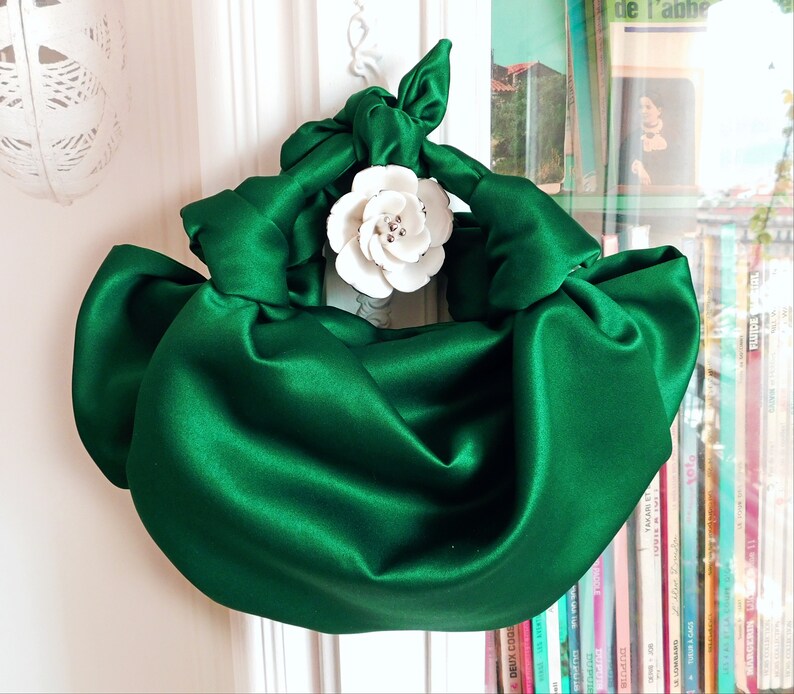 May include: A green satin handbag with a white flower accent. The bag is gathered and knotted to create a unique shape.