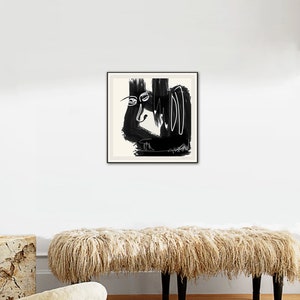 May include: Black and white abstract art print in a black frame, hanging on a white wall above a fluffy beige bench.