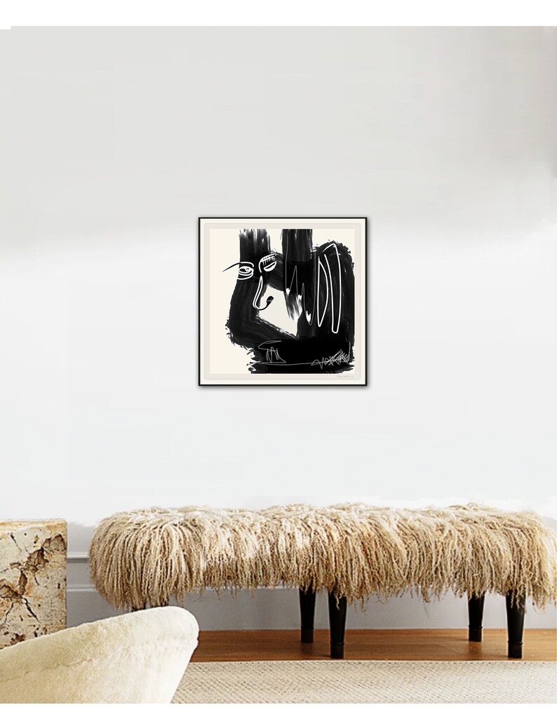 May include: Black and white abstract art print in a black frame, hanging on a white wall above a fluffy beige bench.