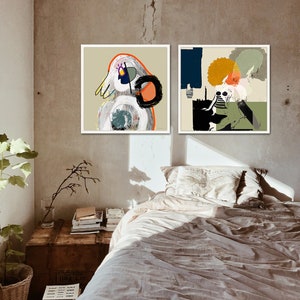 May include: Two framed abstract paintings with colourful geometric shapes and figures hang on a light brown wall above a bed with a white pillow and a beige blanket.