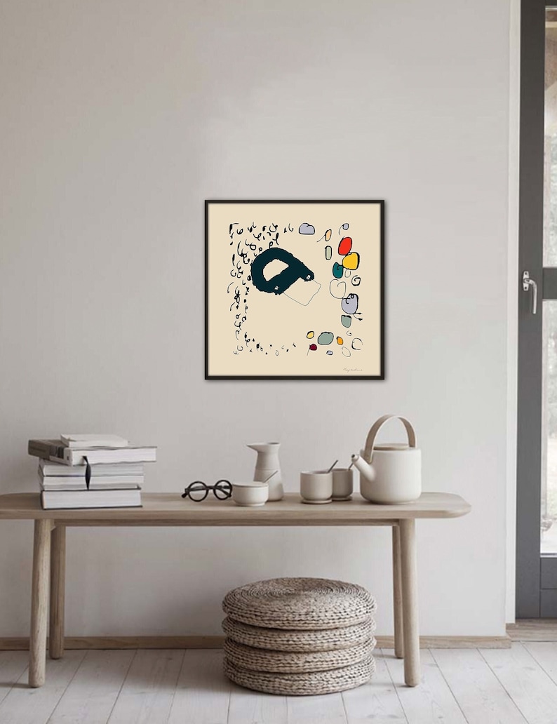 May include: A framed abstract art print with black lines and colorful circles on a cream background. The print is hanging on a white wall above a wooden table with a stack of books, a teapot, and a bowl.