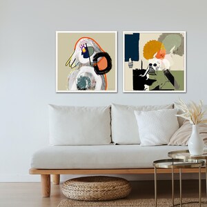 May include: Two framed abstract art prints with white frames. The print on the left features a white, grey, and orange abstract figure. The print on the right features a white, grey, green, and yellow abstract figure.