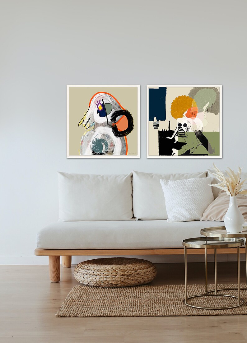 May include: Two framed abstract art prints with white frames. The print on the left features a white, grey, and orange abstract figure. The print on the right features a white, grey, green, and yellow abstract figure.