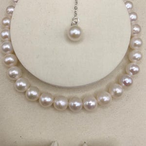 May include: A pearl necklace and matching earrings set. The necklace is a strand of round, white pearls. A single pearl pendant hangs from a delicate silver chain. The earrings are also pearl studs. The jewelry is displayed on a white background.