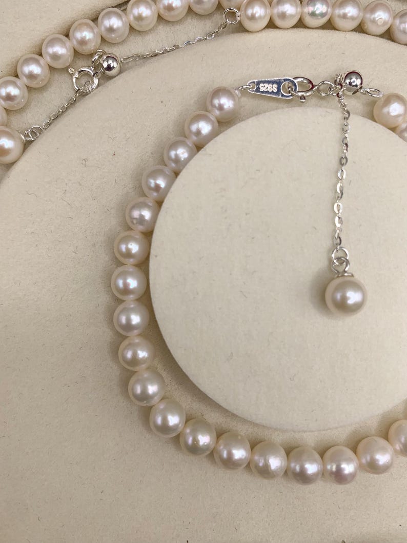 May include: A delicate pearl necklace with a silver clasp and adjustable chain. The necklace features numerous round, creamy white pearls. The clasp is marked with "S925". The necklace is displayed on a neutral background.