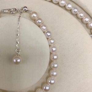 May include: A delicate pearl necklace and bracelet set. The jewelry features lustrous, off-white pearls strung together with a silver chain and clasp. The bracelet is partially visible, showcasing the round pearls and the adjustable chain.