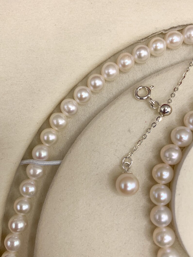 May include: A delicate pearl necklace with a matching pendant. The necklace features a strand of lustrous, round pearls. The pendant hangs from a fine silver chain. The pearls have a soft, creamy white color.