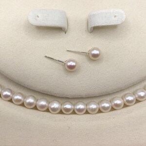 May include: A jewelry set featuring a necklace, stud earrings, and a bracelet, all made with lustrous, round, white pearls. The earrings are displayed on a white background, and the necklace and bracelet are partially visible.