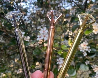 May include: Three diamond-shaped pens with gold, silver, and rose gold finishes. The pens have a clear diamond-shaped top and a metal body.