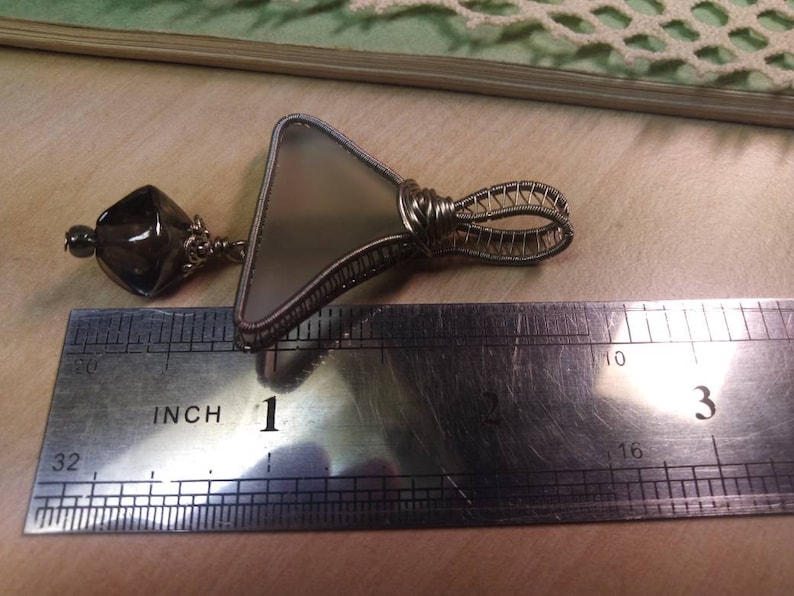 Unique triangular pendant with a pale sea glass wrapped in silver coated copper wire and a smokey glass bead dangling under.