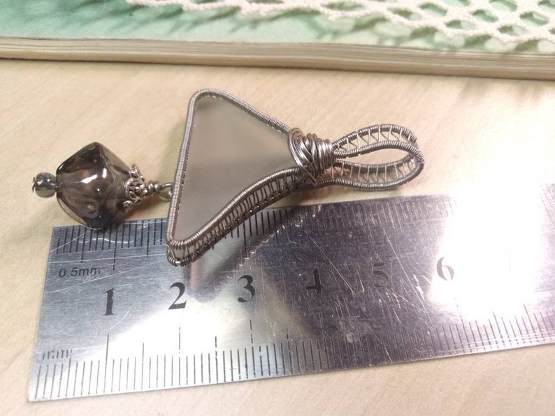 Unique triangular pendant with a pale sea glass wrapped in silver coated copper wire and a smokey glass bead dangling under.