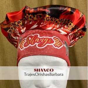 K&ouml;nnte beinhalten: Ein roter, schwarzer und wei&szlig;er Satin-Kopftuch mit Leopardenmuster. Das Kopftuch tr&auml;gt den Schriftzug "Shango" in goldenen Buchstaben. Der Text "TrajesOrishasBarbara" steht unter dem Kopftuch.