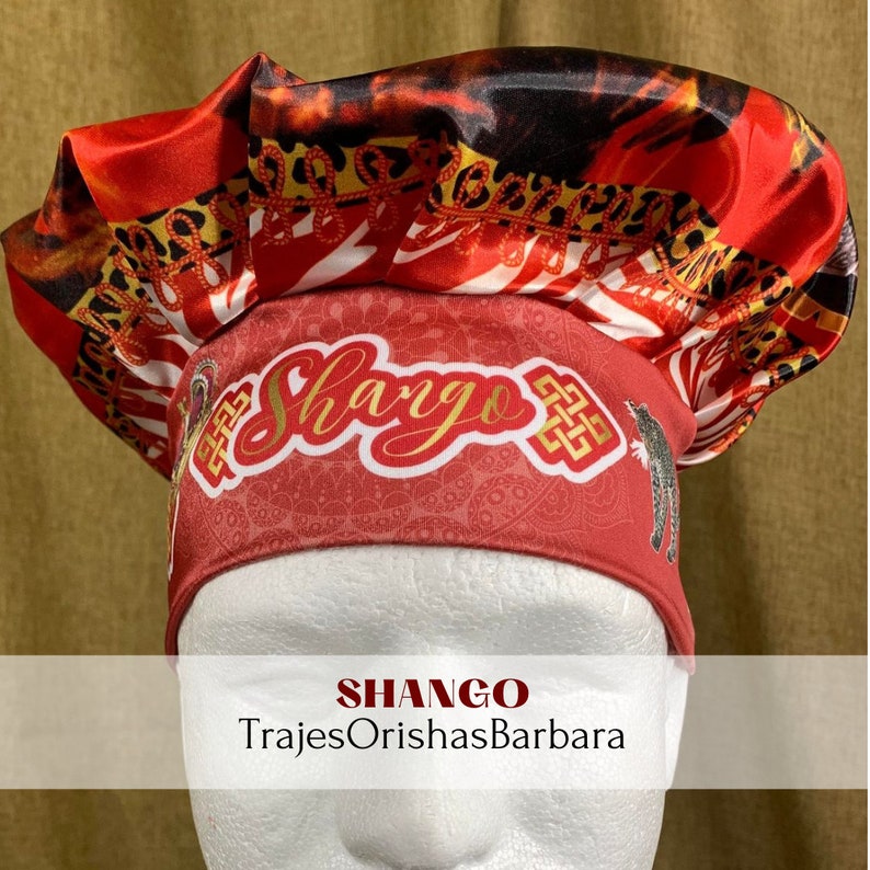 K&ouml;nnte beinhalten: Ein roter, schwarzer und wei&szlig;er Satin-Kopftuch mit Leopardenmuster. Das Kopftuch tr&auml;gt den Schriftzug "Shango" in goldenen Buchstaben. Der Text "TrajesOrishasBarbara" steht unter dem Kopftuch.