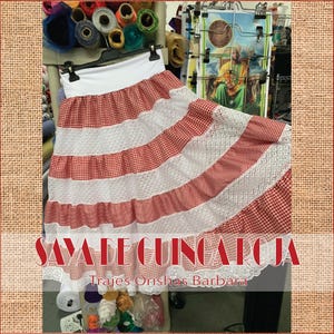May include: A red and white gingham skirt with white lace trim. The skirt is layered and has a white waistband. The text "Saya de Guinga Roja" and "Trajes Orishas Barbara" is visible at the bottom of the image.