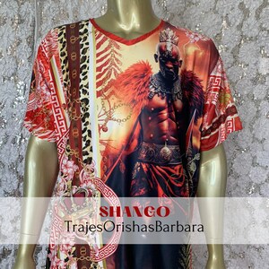 May include: Red, white, and gold short-sleeved t-shirt with a graphic print of a warrior figure. The shirt has a V-neck and features the text "SHANGO" and "TrajesOrishasBarbara".