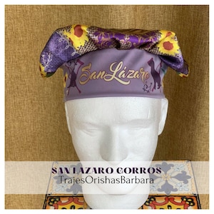 Pode incluir: Chapéu de cozinheiro roxo e amarelo com o texto "San Lazaro" impresso nele. O chapéu está em uma cabeça de manequim branca. O texto "San Lazaro Gorros TrajesOrishasBarbara" está impresso abaixo da cabeça do manequim.