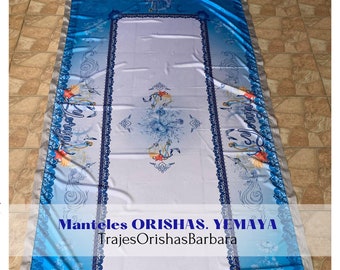 Puede incluir: Un mantel blanco con un borde azul y un diseño floral. El mantel tiene el texto "Manteles ORISHAS. YEMAYA" y "TrajesOrishasBarbara" impreso en él.