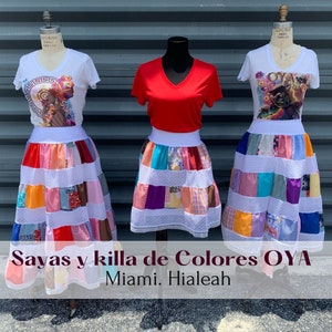 May include: Three colorful patchwork skirts with white lace trim and white tops. The tops have different designs, one with a red v-neck, one with a graphic of a woman's face, and one with a graphic of a woman's face with a crown. The text "Sayas y killa de Colores OYA Miami. Hialeah" is at the bottom of the image.