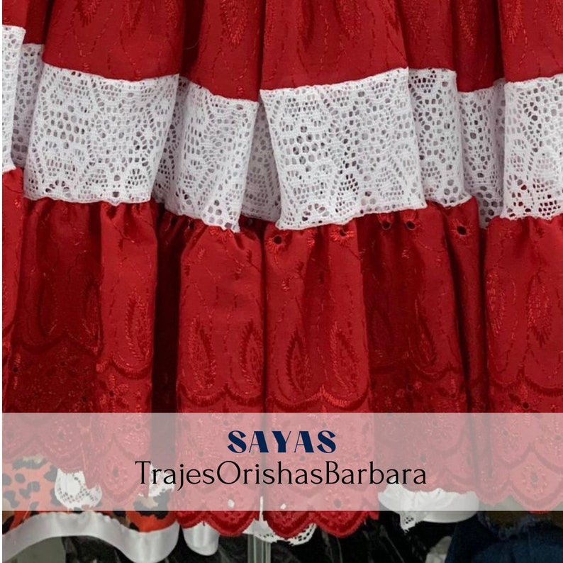 May include: Red skirt with white lace trim. The skirt has a scalloped edge and is embroidered with a floral design. The text "SAYAS TrajesOrishasBarbara" is visible at the bottom of the image.