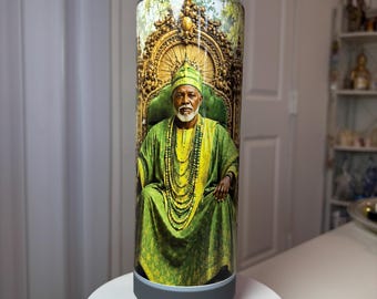 May include: A cylindrical tumbler featuring a full-wrap graphic of an older person with a white beard, wearing a green and yellow traditional robe, a matching cap, and layered beaded necklaces, seated on an ornate gold-colored throne.