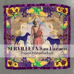 May include: Purple satin fabric with a gold and brown design featuring a saint, two dogs, corn, and sunflowers. The text "Servilleta San Lazaro" and "Trajes Orishas Barbara" is printed on the fabric.