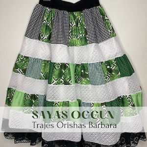 May include: A multi-layered skirt with a black waistband. The skirt is made of green and white fabric with a checkered pattern and a tropical leaf print. The skirt has a lace trim at the bottom. The text "Sayas OgguN Trajes Orishas Barbara" is printed on the skirt.